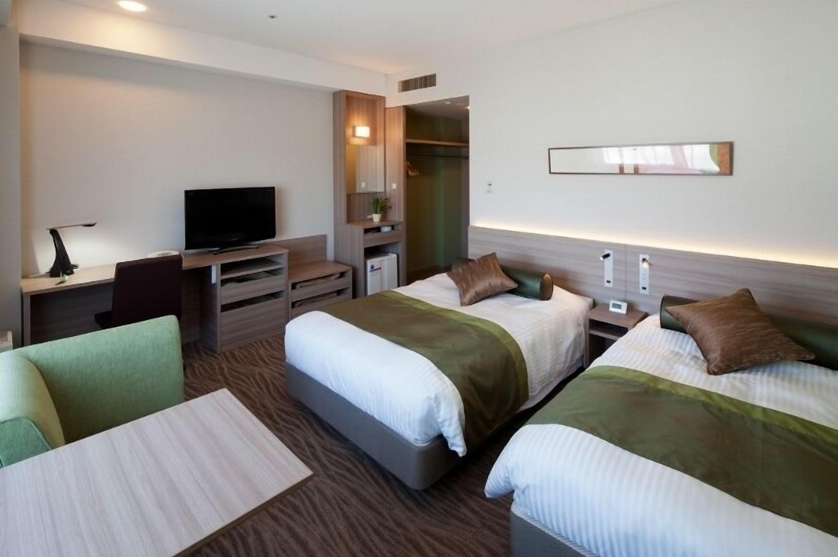A hotel room with two beds, a TV, a desk, and a chair.