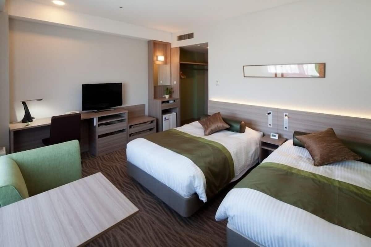 A hotel room with two beds, a TV, a desk, and a chair.