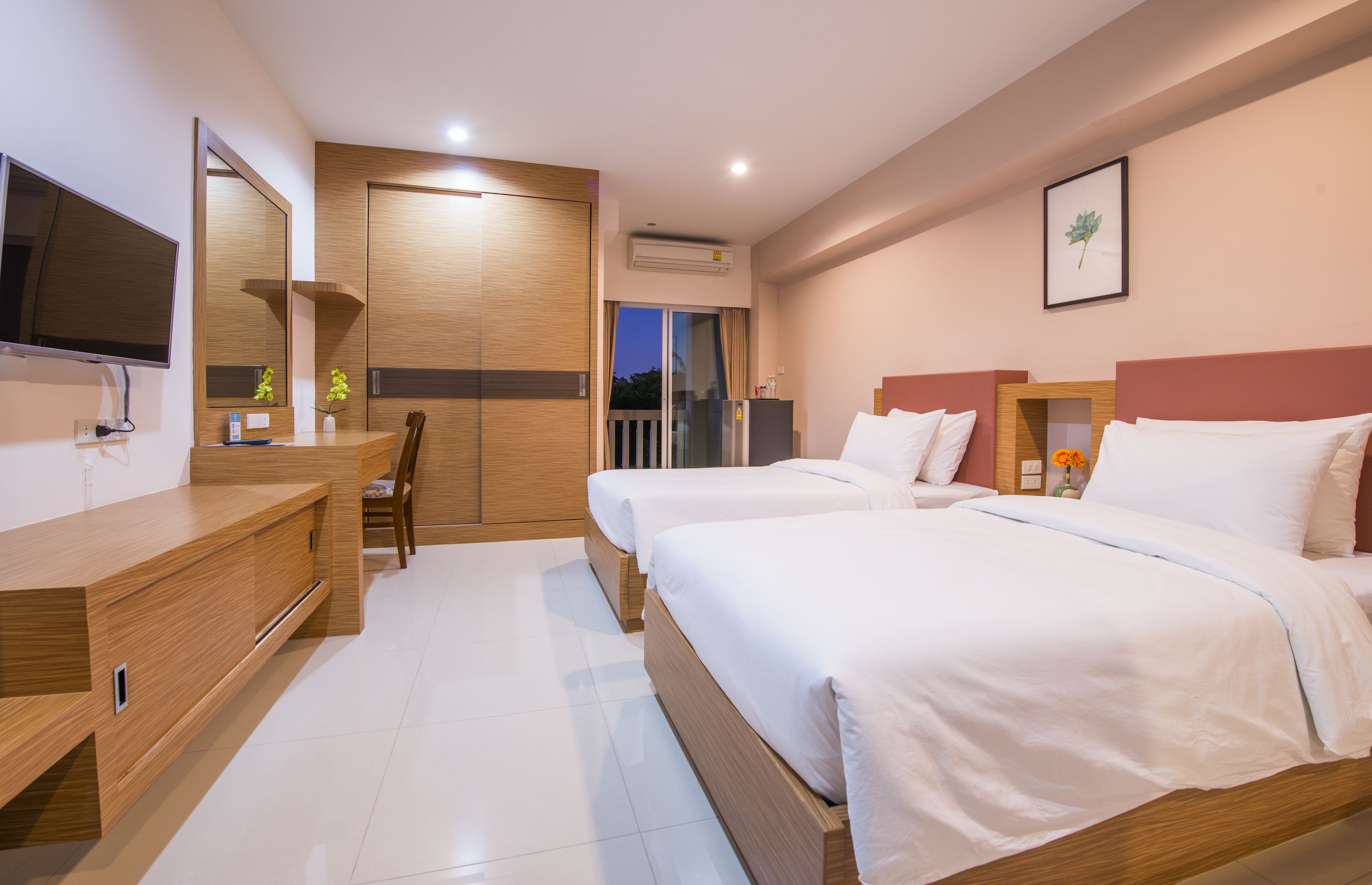 A hotel room with two beds, a TV, a wooden dresser, and a balcony with a view.