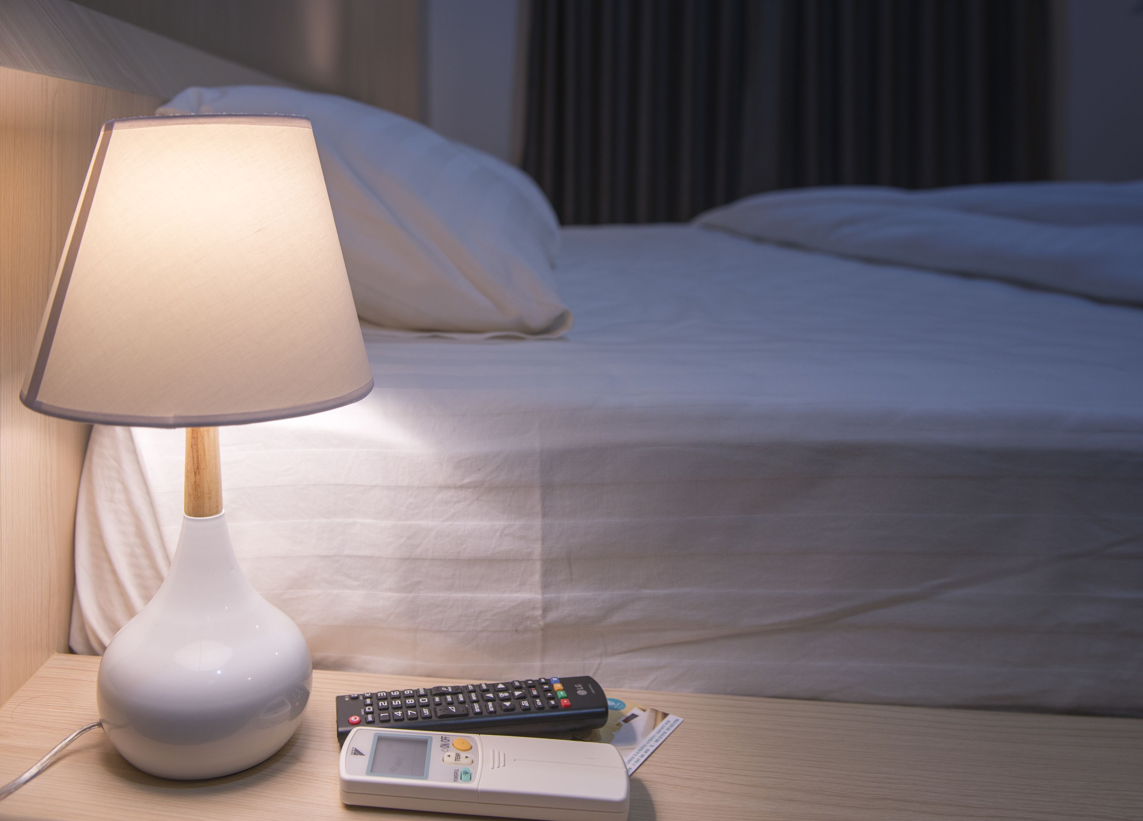 A hotel room with a bedside lamp, a remote control, and a mobile phone on the nightstand.