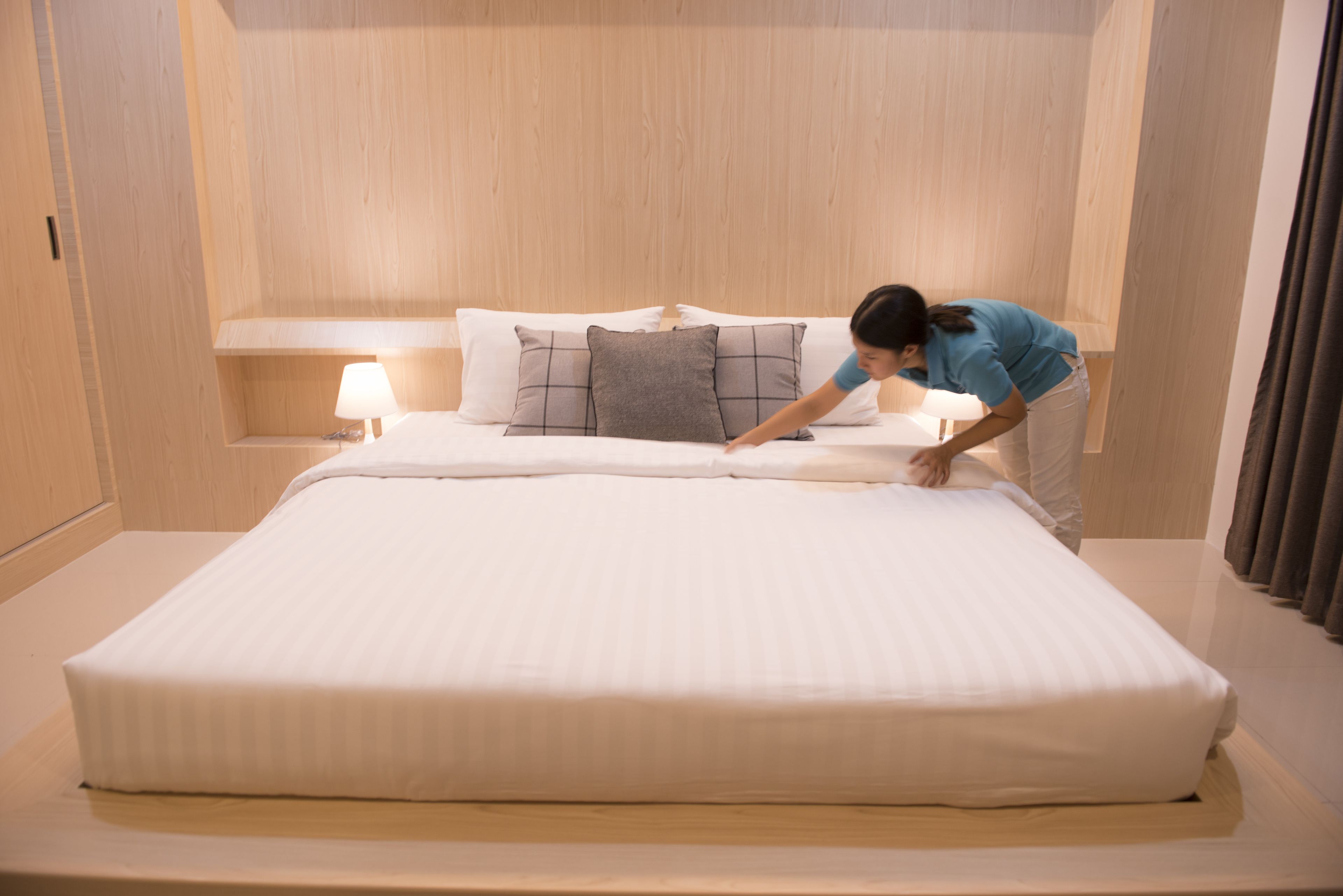 A neatly made bed with pillows and a bedside lamp in a room with wooden paneling.