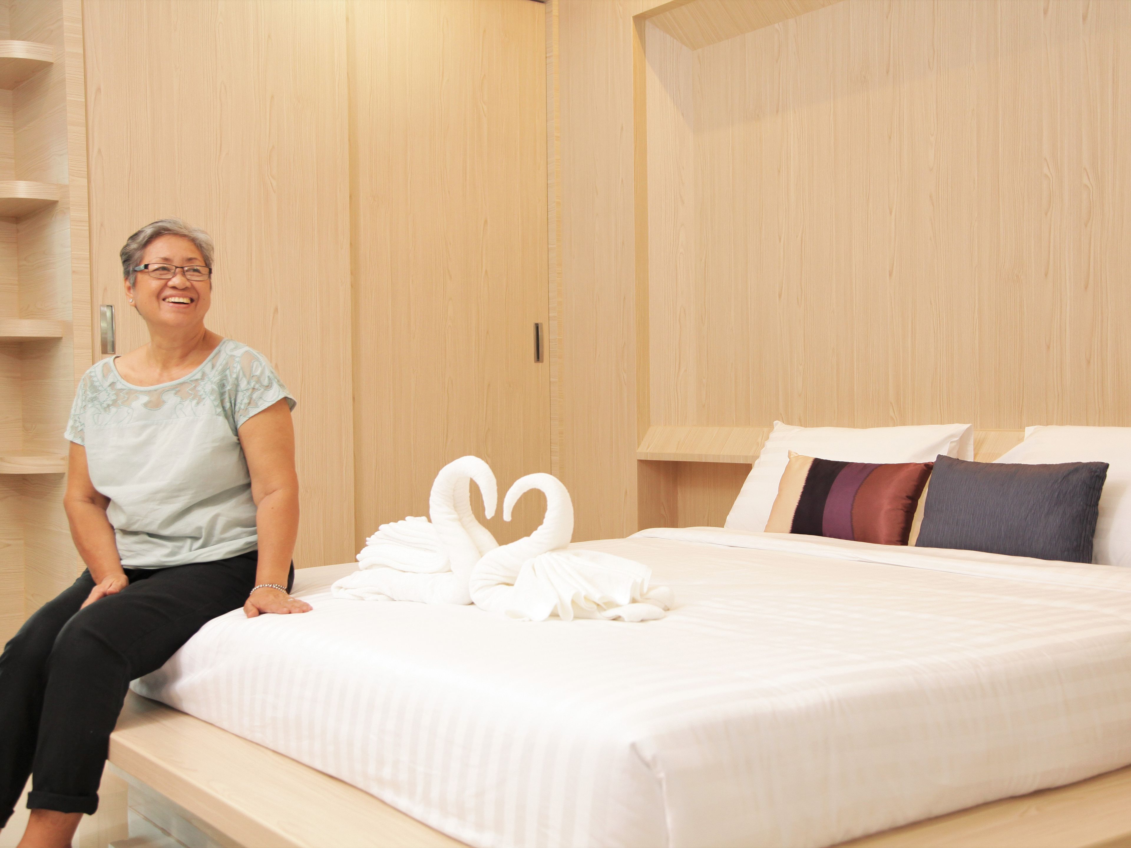 A hotel room with a bed, a wooden wardrobe, and a person sitting on the bed.