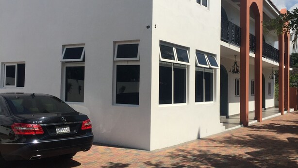 Un edificio moderno con fachada blanca, múltiples ventanas y un coche negro estacionado adelante.