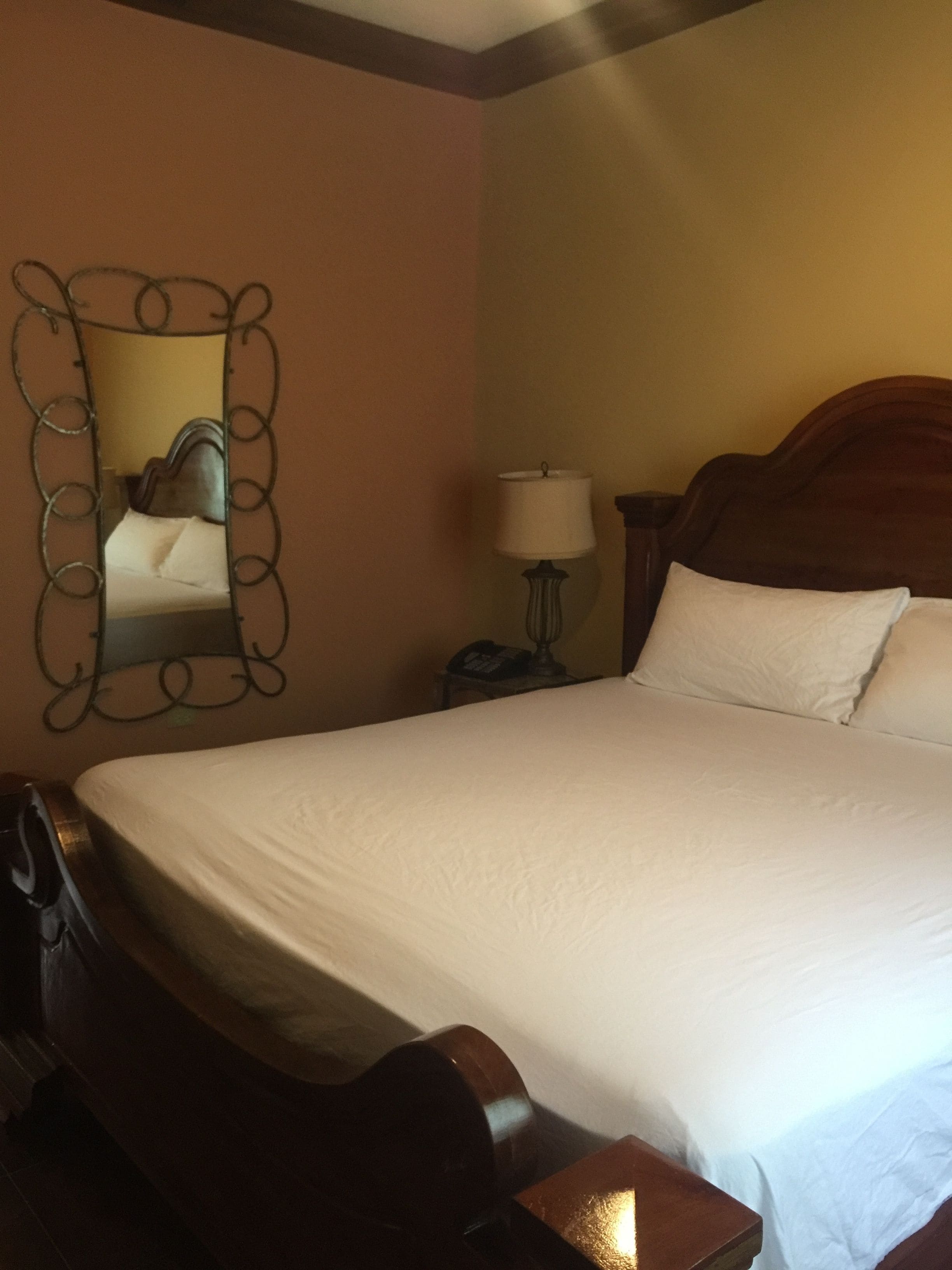 Une chambre d’hôtel avec un grand lit, une tête de lit en bois, une table de chevet avec une lampe et un miroir doté d’un cadre décoratif.