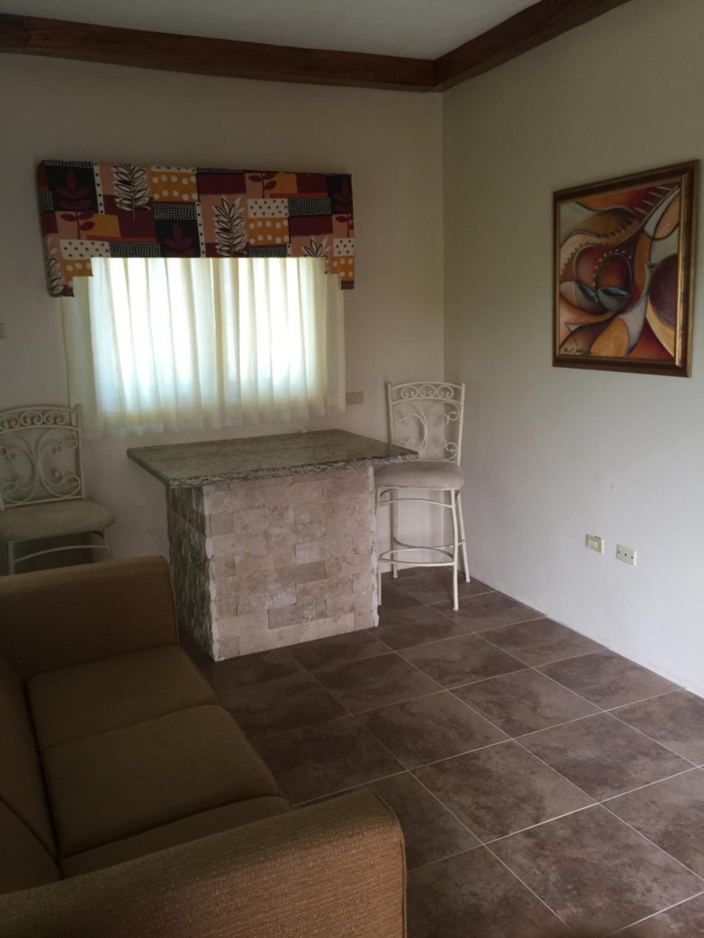 A living room with a sofa, a small dining area with a table and chairs, a decorative wall hanging, and a painting.
