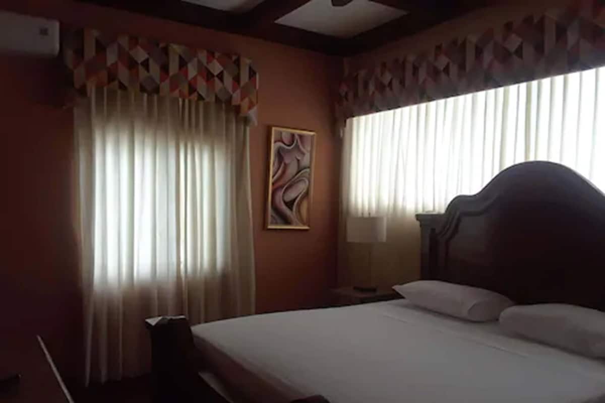 A hotel room with a bed, curtains, a painting, and a nightstand.
