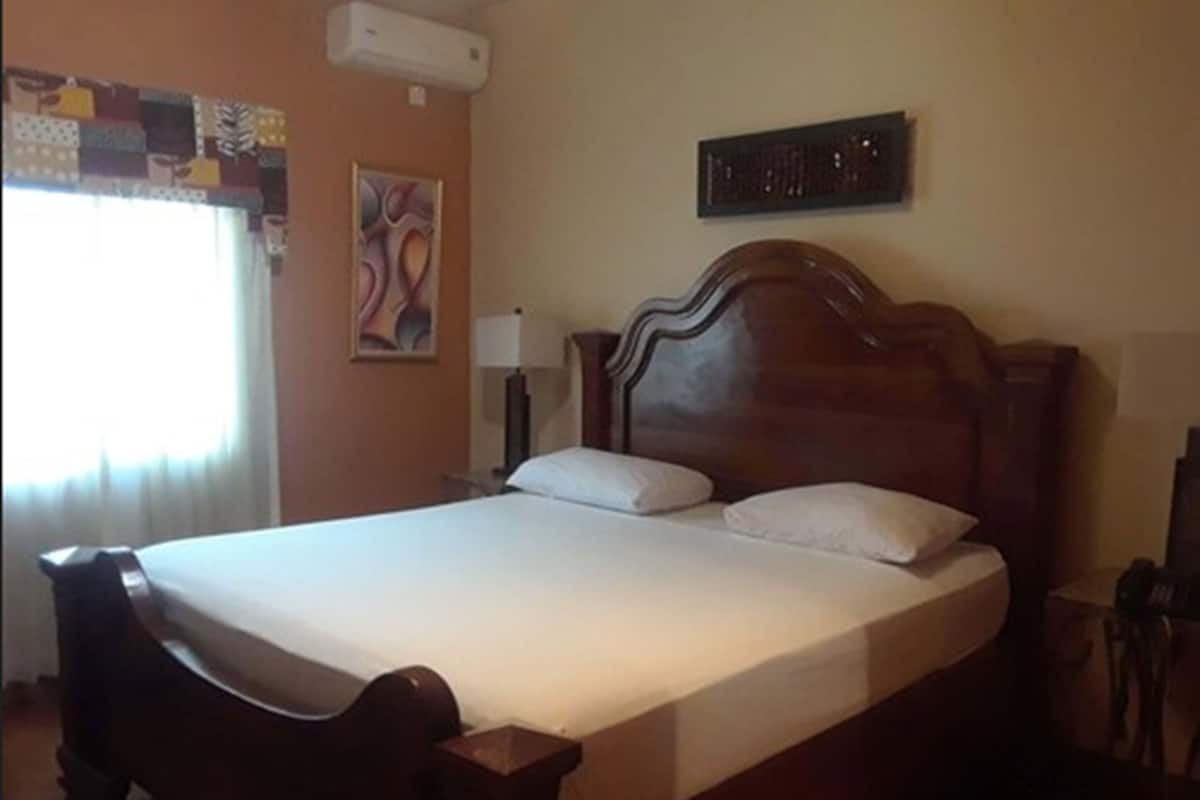 A bedroom with a wooden bed, a nightstand, a lamp, and a wall-mounted air conditioner.