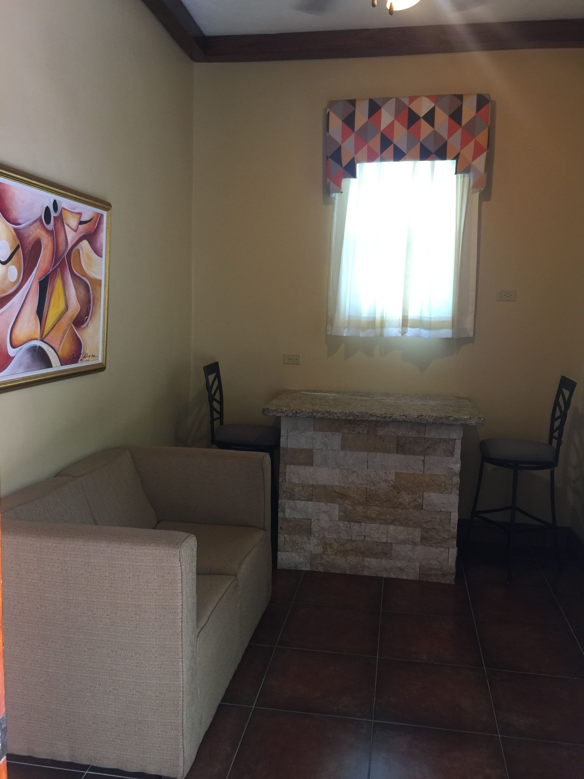 Una sala de estar con un sofá color crema, una chimenea de piedra y un ventanal con cortina de diseño geométrico.