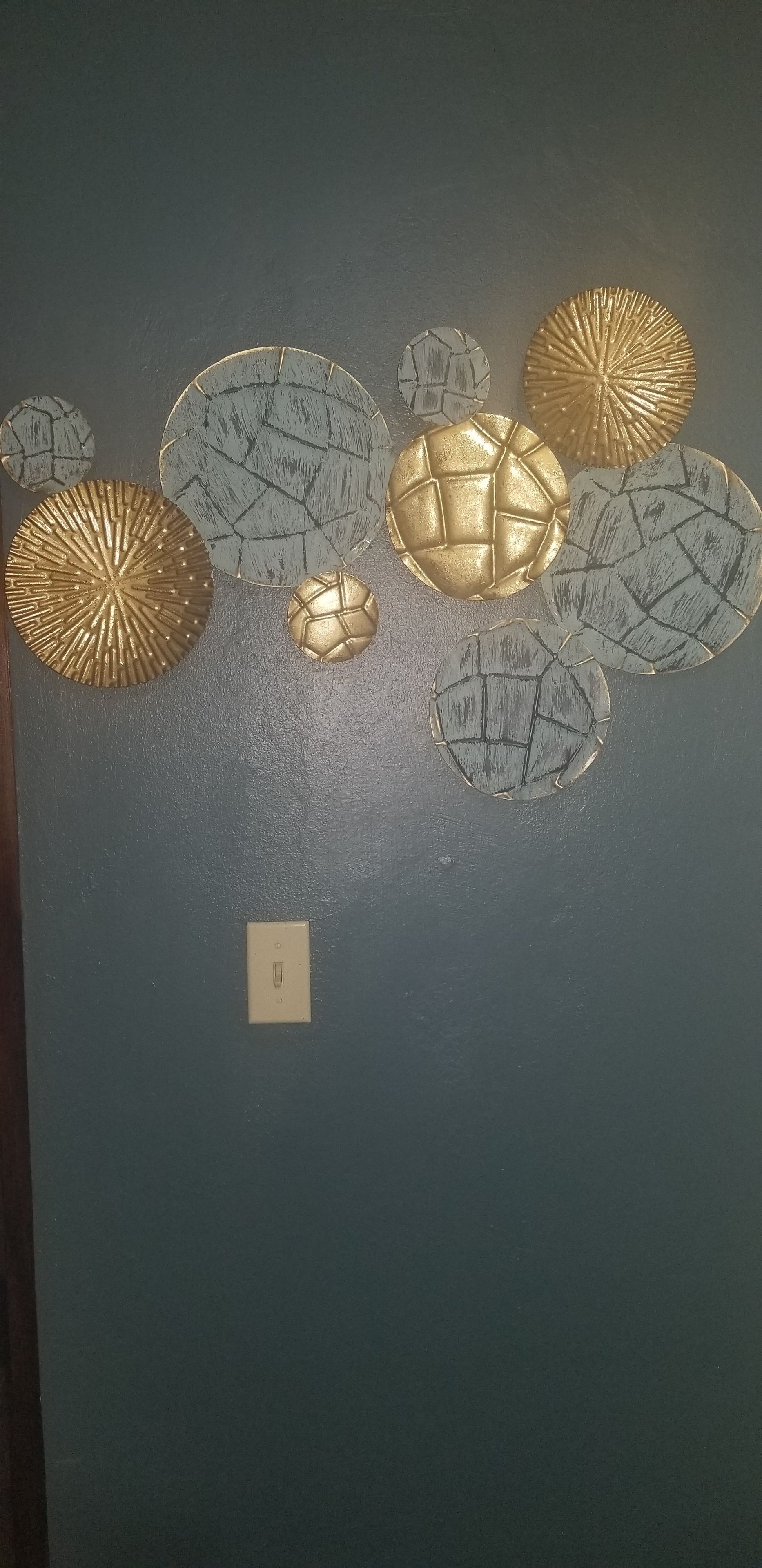 Een muur met diverse decoratieve borden, waaronder een grote gouden voetbal en kleinere borden met verschillende patronen.