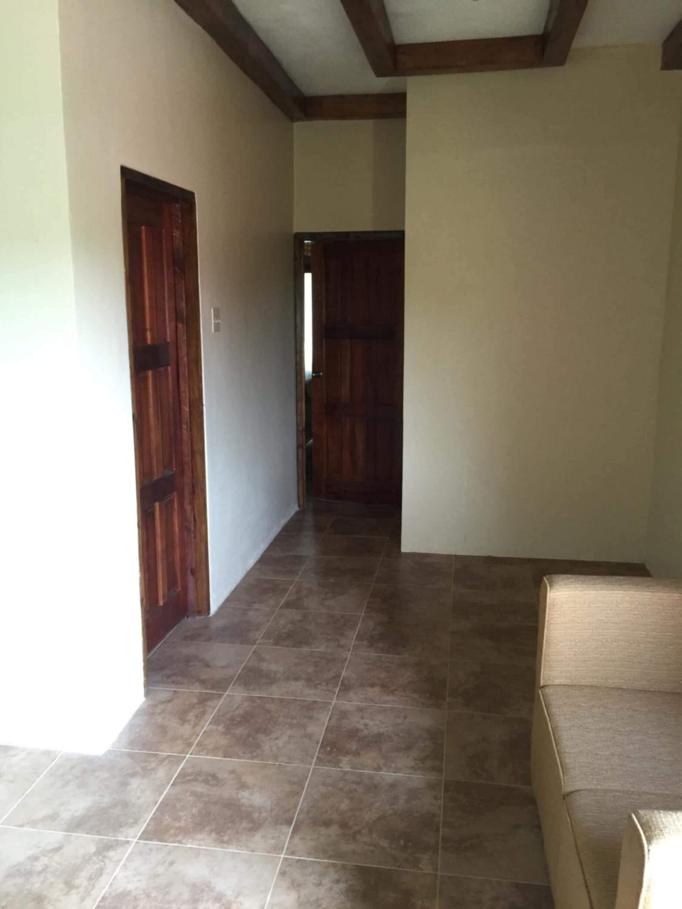 Un pasillo con suelo de baldosas, puertas de madera y un sofá color beige.