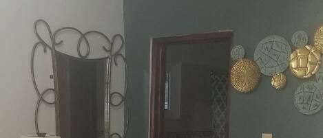 A bedroom with a bed, a nightstand, a lamp, a mirror, and a bathroom visible through an open door.