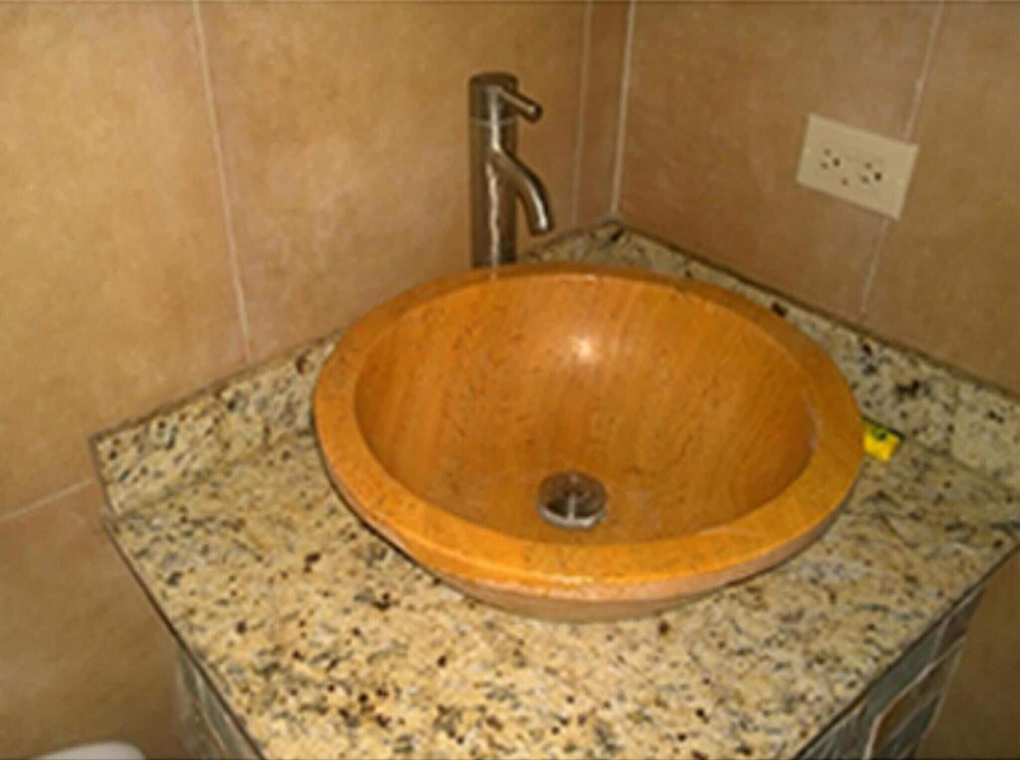 A bathroom with a wooden sink, granite countertop, and a wall-mounted faucet.