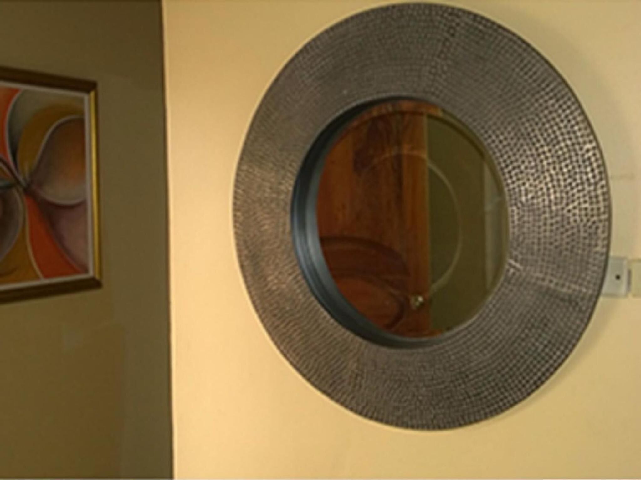 A round mirror with a textured frame on a wall.