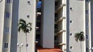 A multi-story building with balconies, a parking lot, and a clear blue sky.