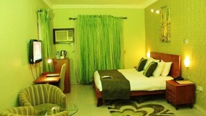 A hotel room with a bed, bedside table, lamp, chair, desk, and a television. - Vines Hotel (Abuja)