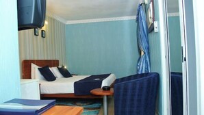 A compact hotel room with a bed, a small table, a chair, and a TV mounted on the wall. - Vines Hotel (Abuja)