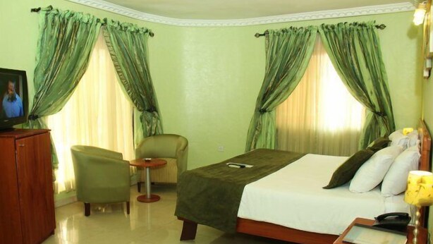 A hotel room with a bed, a chair, a small table, and curtains. - Vines Hotel (Abuja)