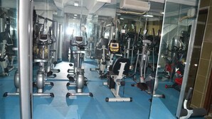 Een sportschool met diverse fitnessapparaten, een blauwe vloer en een grote spiegelwand.