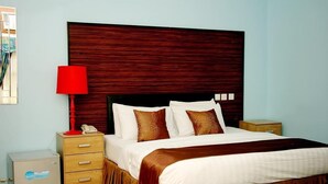 Een hotelkamer met een groot bed, een houten hoofdbord, een rode lamp, een nachtkastje en een klein kastje.