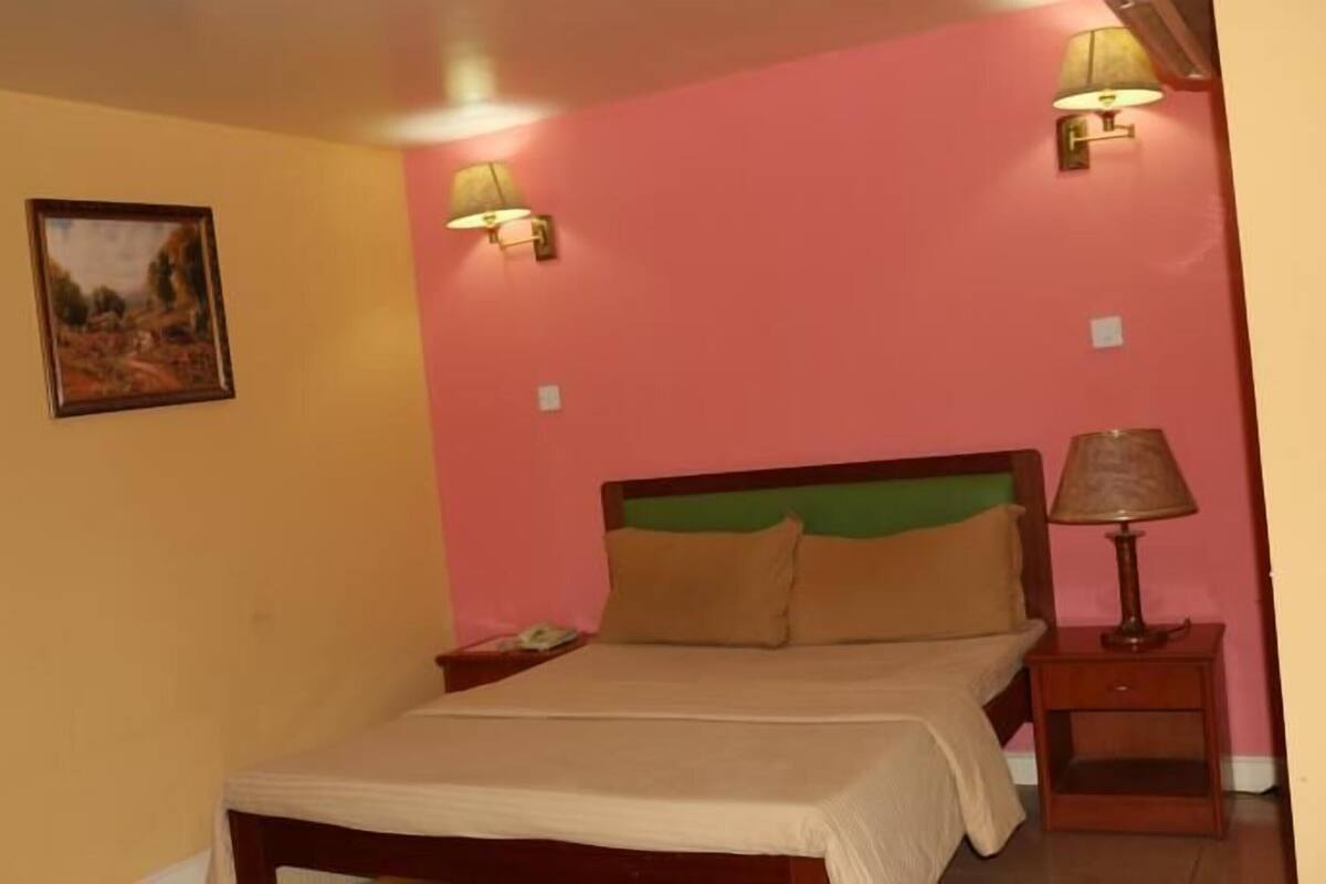 A bedroom with a bed, two bedside lamps, a nightstand, a wall-mounted painting, and a red accent wall.