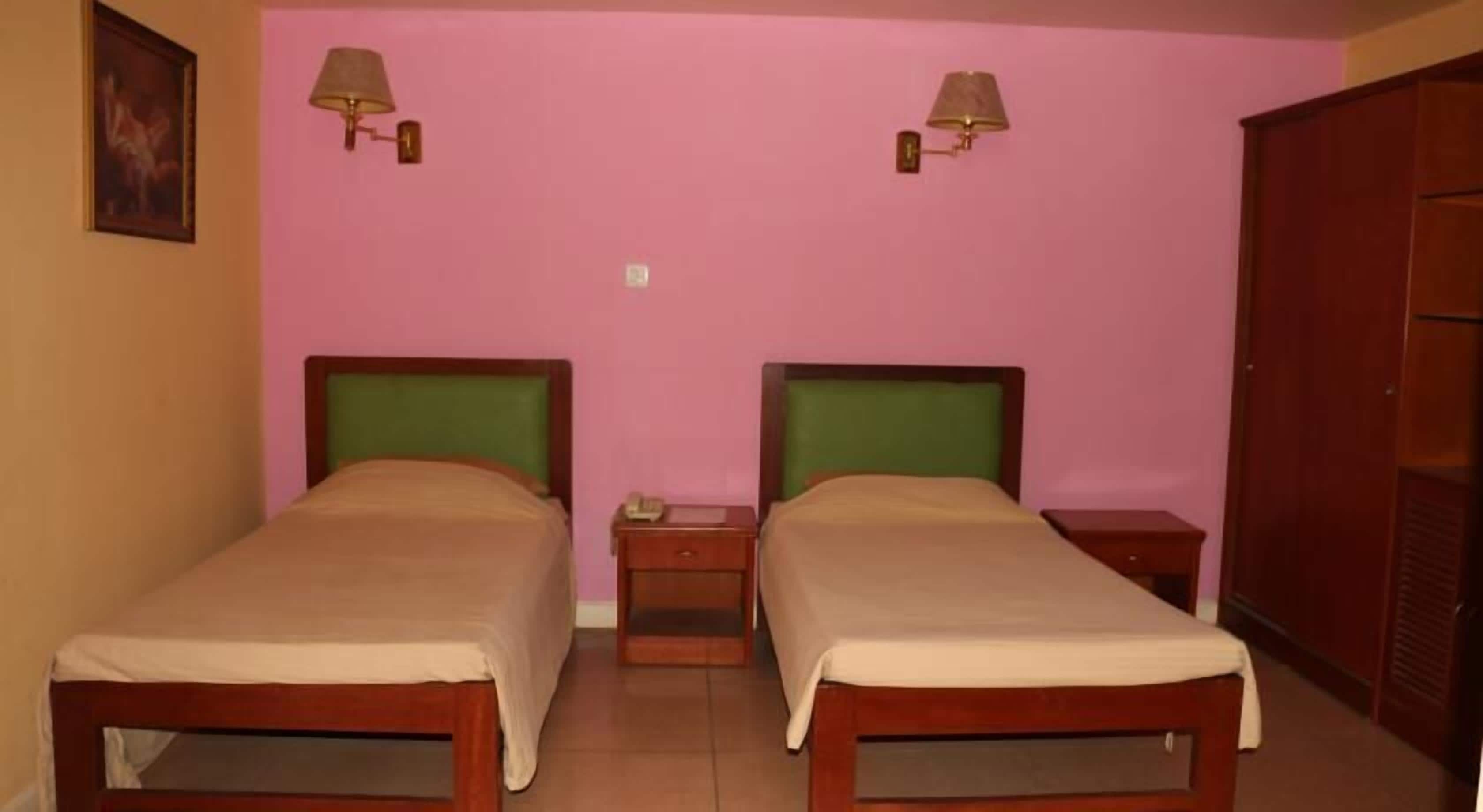 A room with two single beds, a nightstand with a lamp, and a wardrobe.