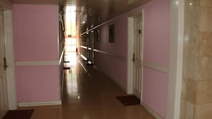 A long, narrow hallway with pink walls and a tiled floor, leading to a bright room at the end. - Golden Gate Hotel Abuja (Abuja)
