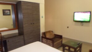 A hotel room with a bed, a wooden wardrobe, a small wooden chair, a television mounted on the wall, and a small table. - Parkview Hotel Abuja (Abuja)