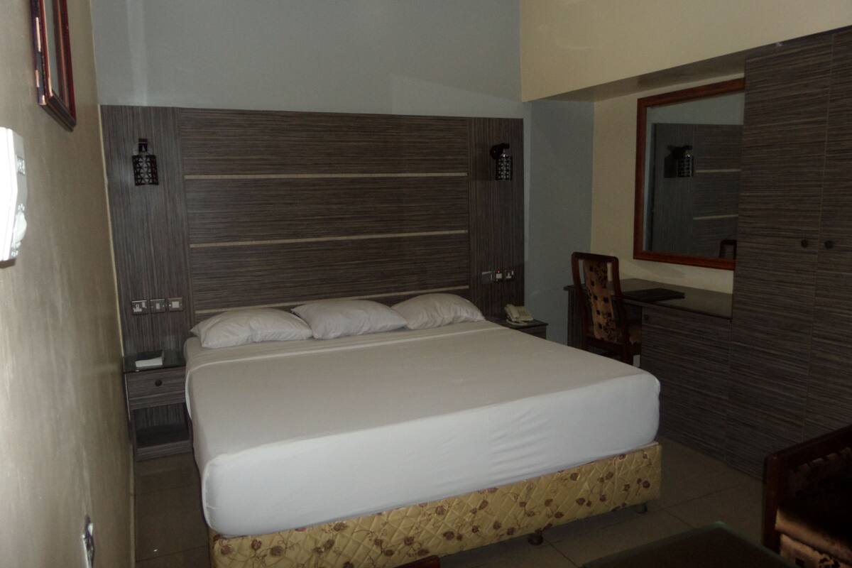 A bedroom with a large bed, a nightstand, a chair, and a mirror on the wall.