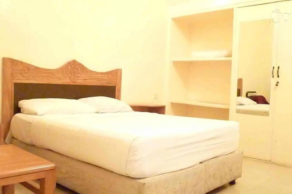 A single bed with a wooden headboard, a bedside table, and a wardrobe with a mirror.
