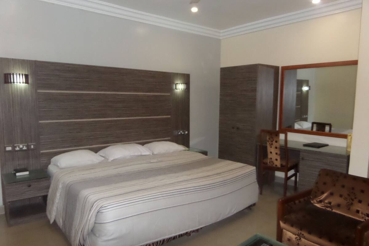 A bedroom with a large bed, a nightstand, a chair, a dresser, and a mirror.