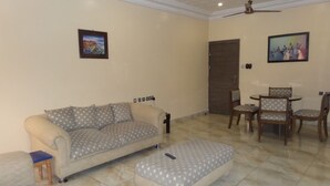 A living room with a sofa, ottoman, and dining table with chairs. - Parkview Hotel Abuja (Abuja)