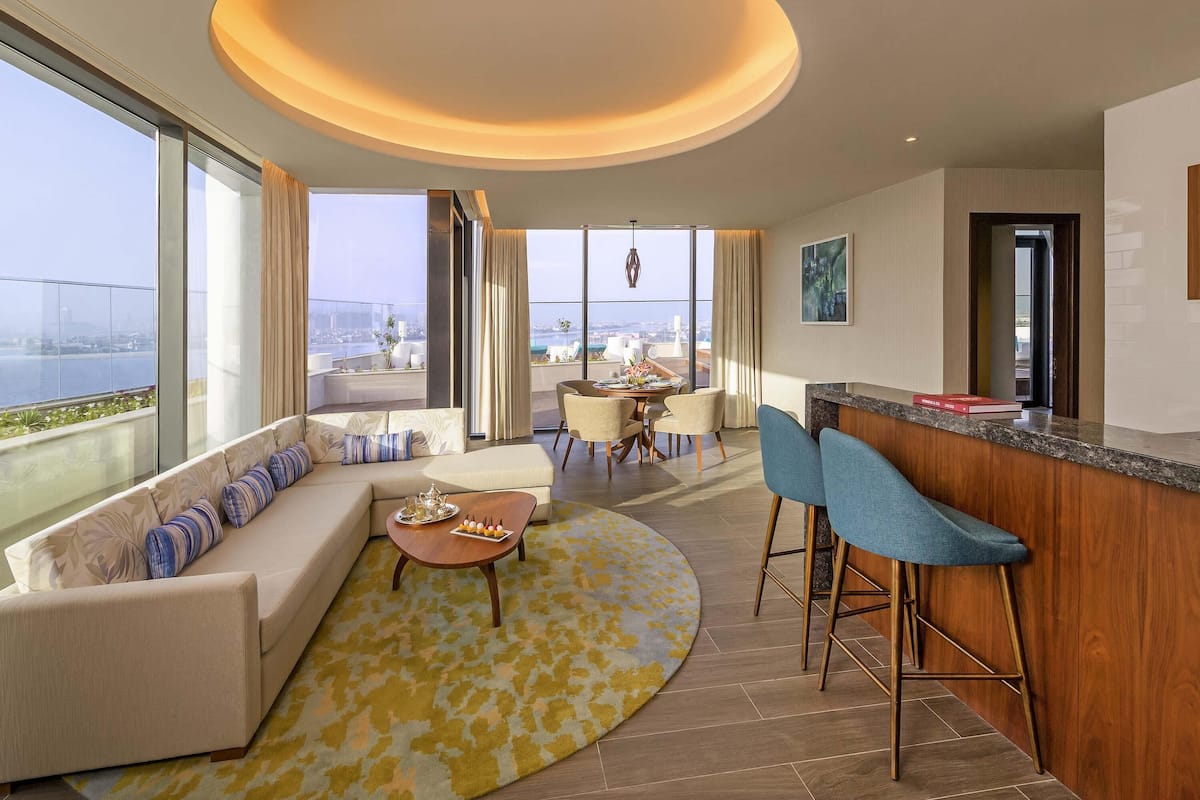 Ein modernes Hotelzimmer mit einer großen Couch, einer Essecke, einer Bar und Blick auf die Stadt.