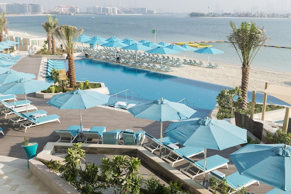 A pool area with lounge chairs and umbrellas, a beach, and a city skyline in the background.