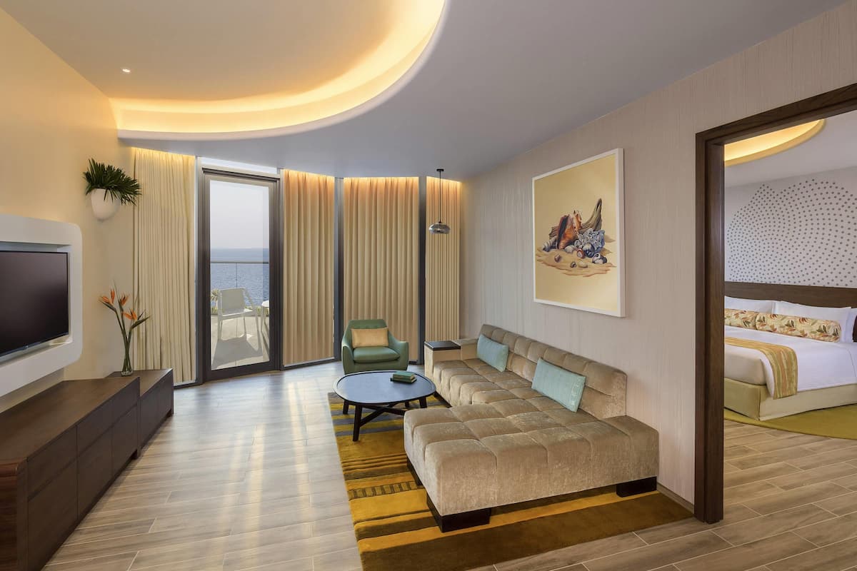 Ein modernes Hotelzimmer mit einer großen Couch, einem Flachbildfernseher, einem Esstisch und einem Balkon mit Vorhängen.