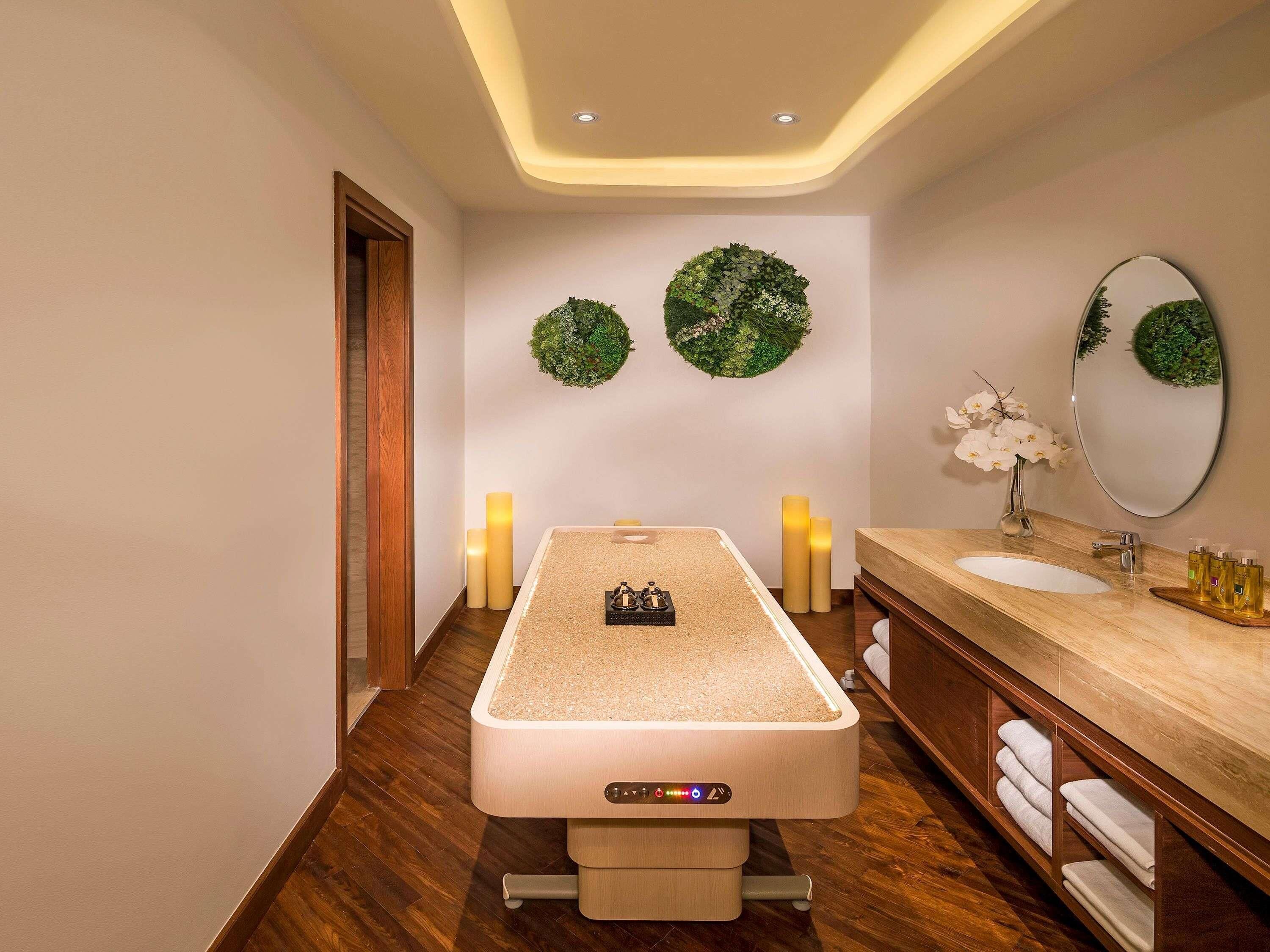 Een moderne badkamer met een centraal geplaatst houten bad, een houten wastafelmeubel met spiegel en twee groene kransen aan de muur.