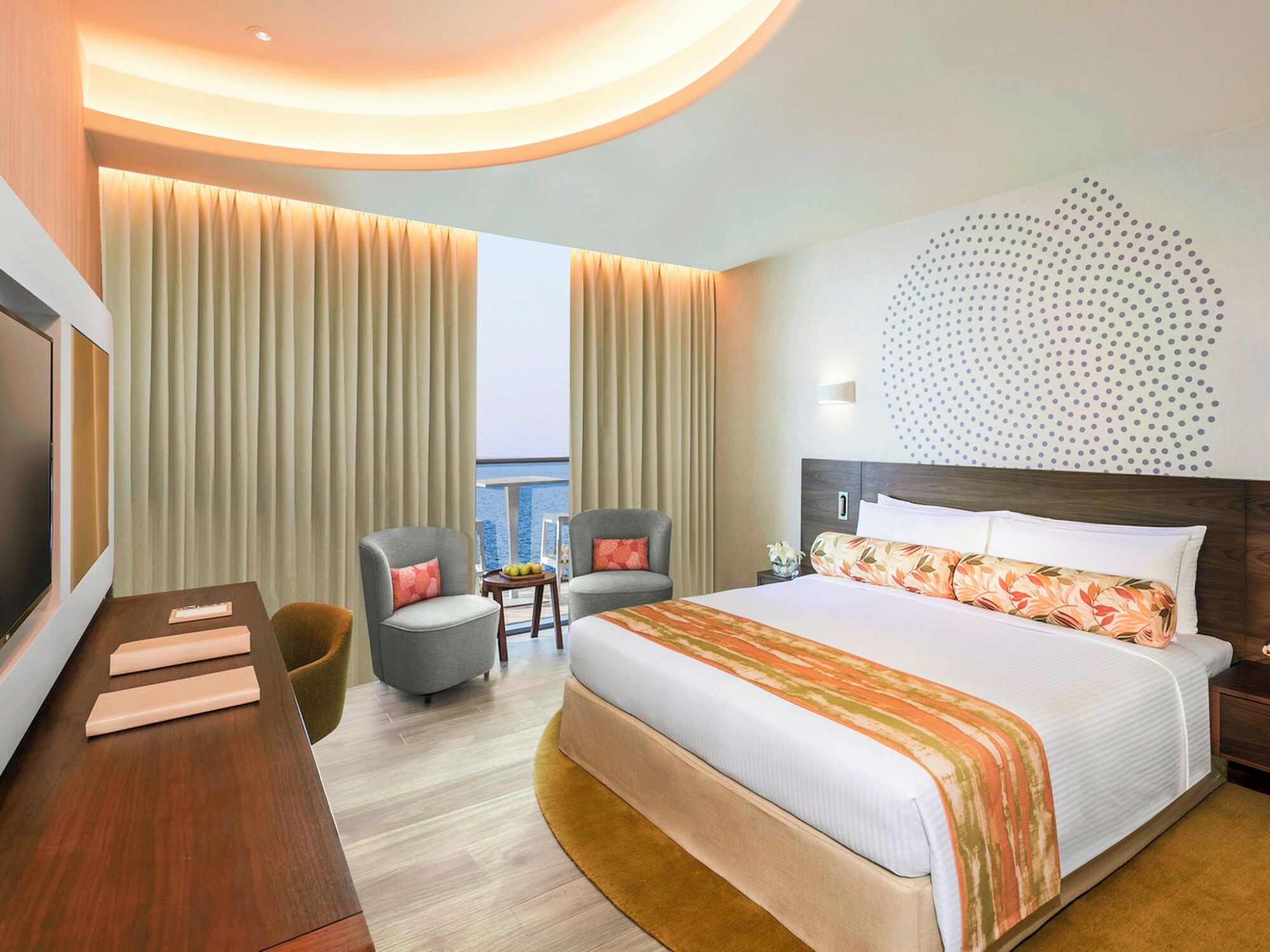 A hotel room with a large bed, two armchairs, a desk, and a TV.