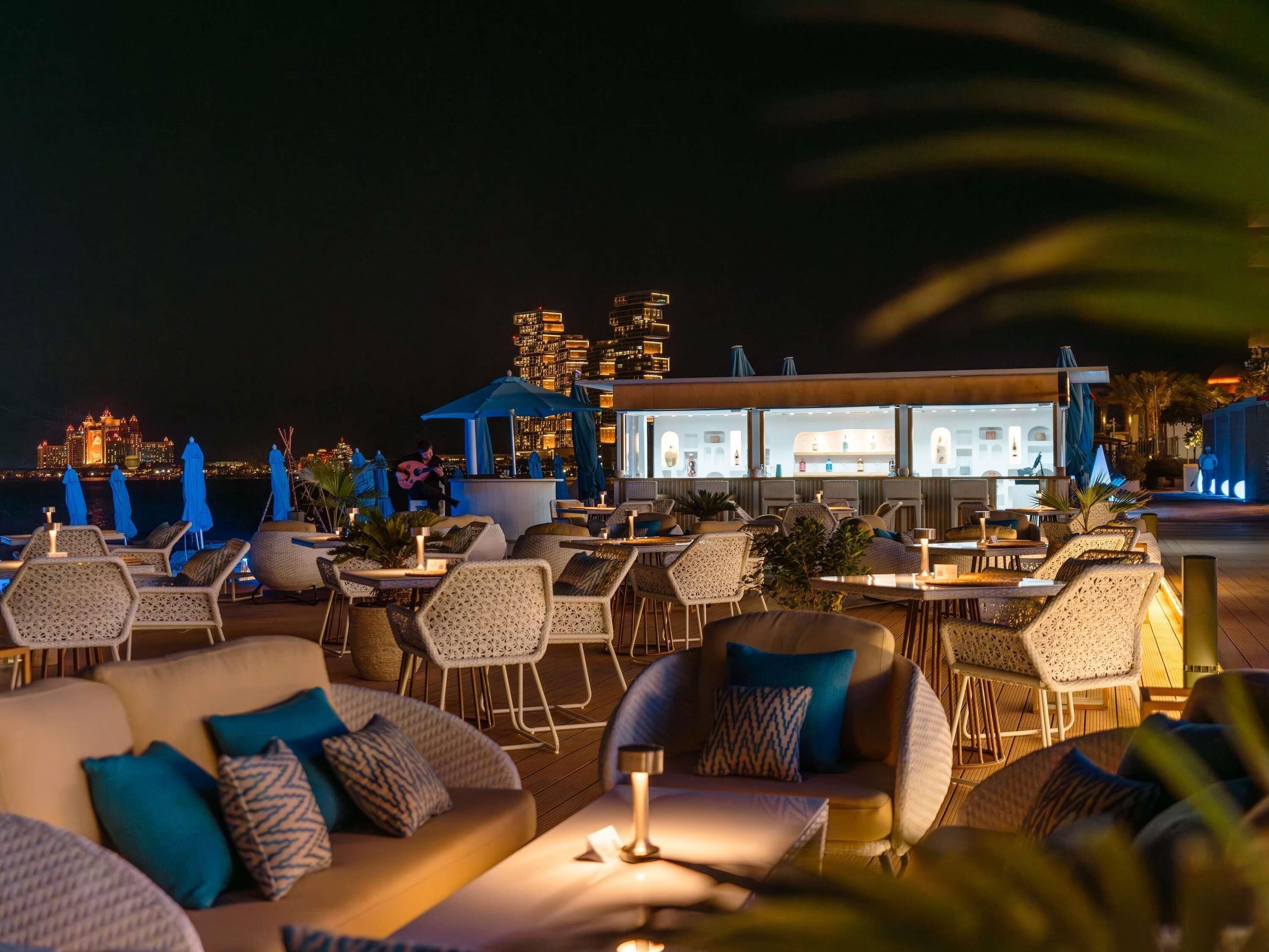 Een dakterras met terras, een uitzicht op een stadshemelbeeld en een bar met verlichte binnenzijde.
