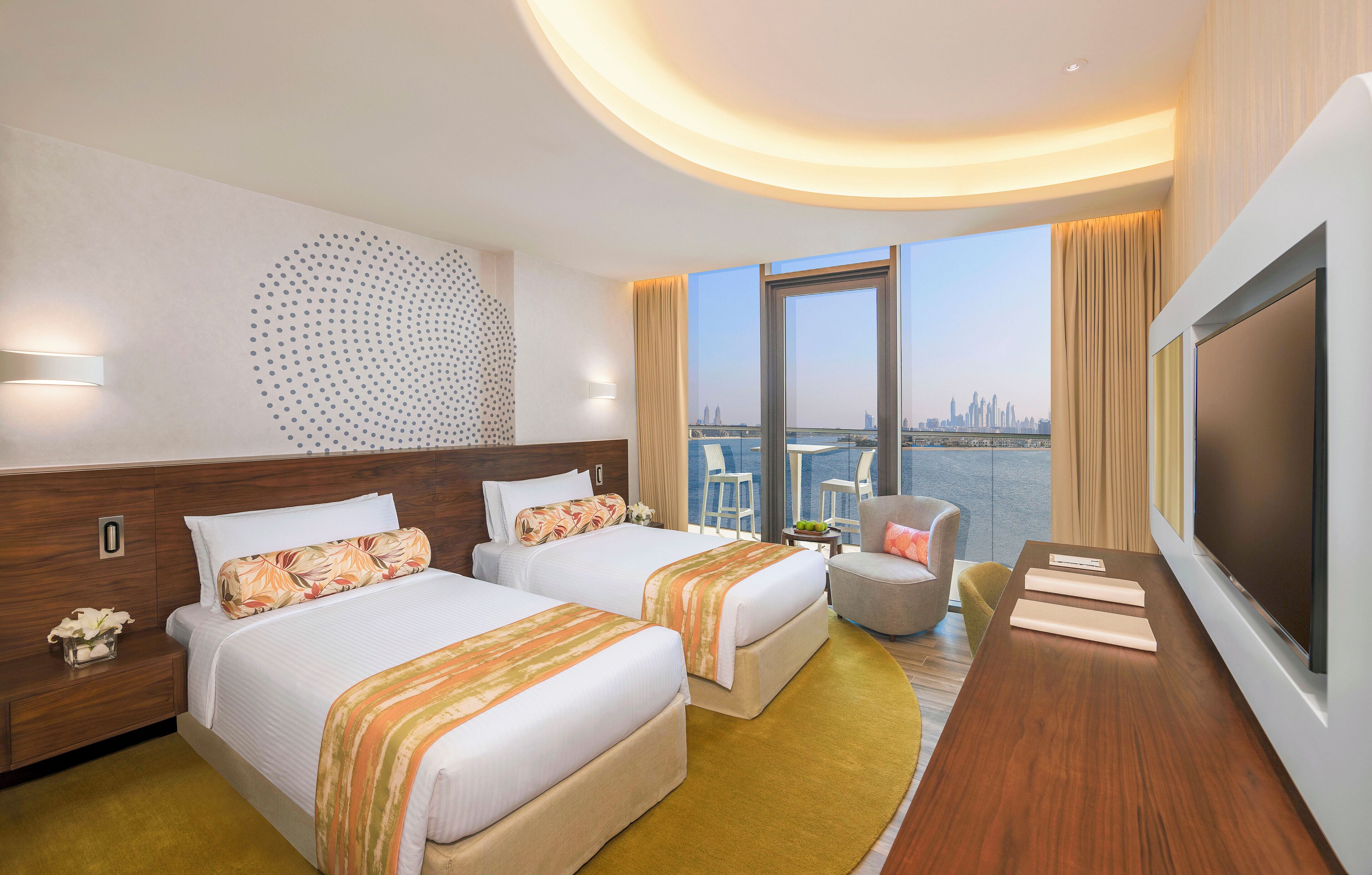 Habitación de hotel con dos camas, televisión, escritorio y vistas a un horizonte urbano.