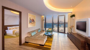 Una habitación de hotel moderna con una cama grande, un sofá, una mesa de centro y un televisor. La habitación tiene un balcón con vistas a la ciudad.