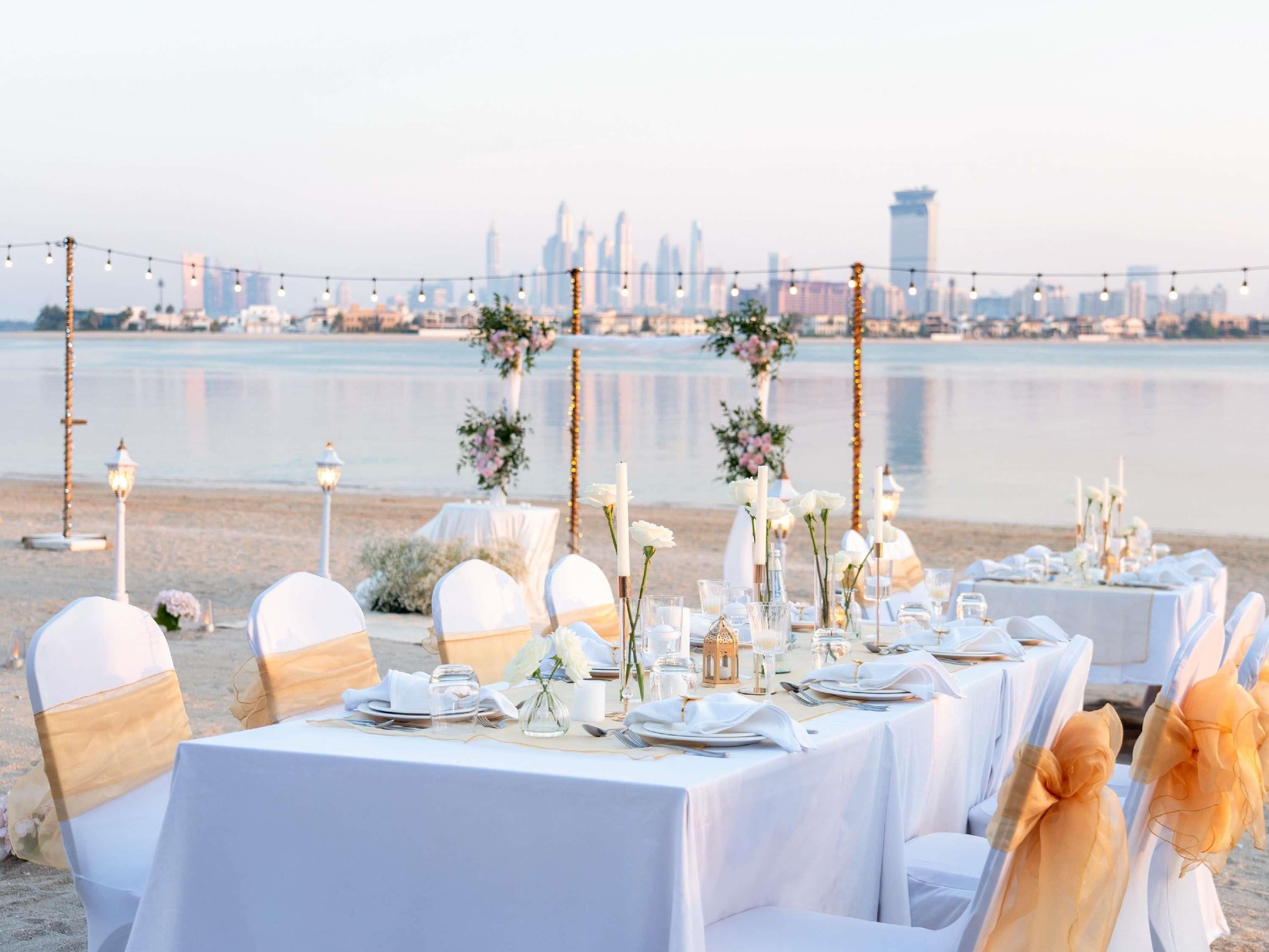 An outdoor wedding setup with tables and chairs, a city skyline in the background, and a body of water.
