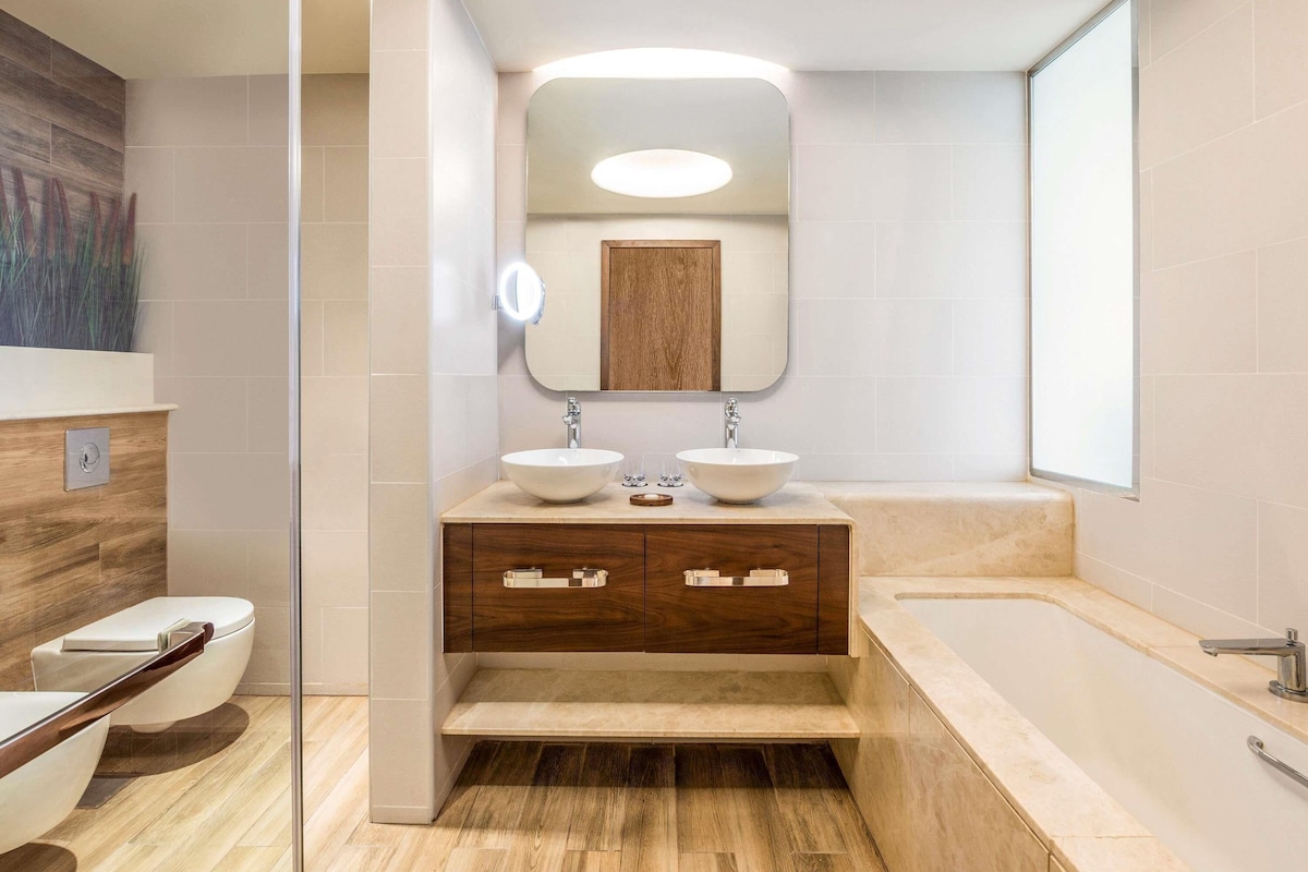 A modern bathroom with a double sink vanity, a large mirror, and a bathtub.