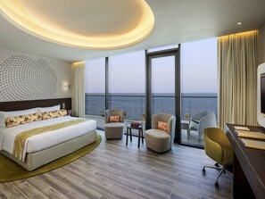 Ein Hotelzimmer mit einem großen Bett, zwei Sesseln, einem Schreibtisch und Meerblick.