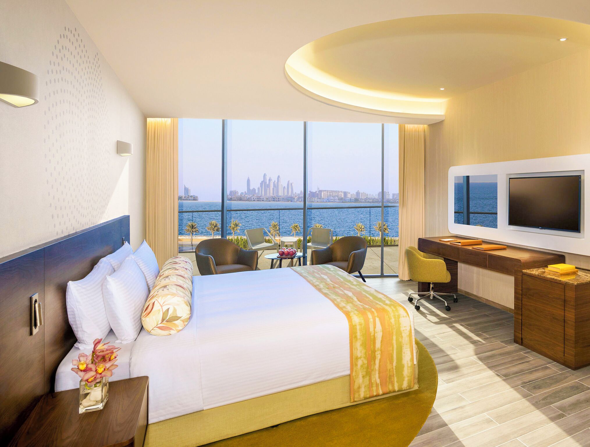 A hotel room with a large bed, a desk, a TV, and a view of the city skyline and water.