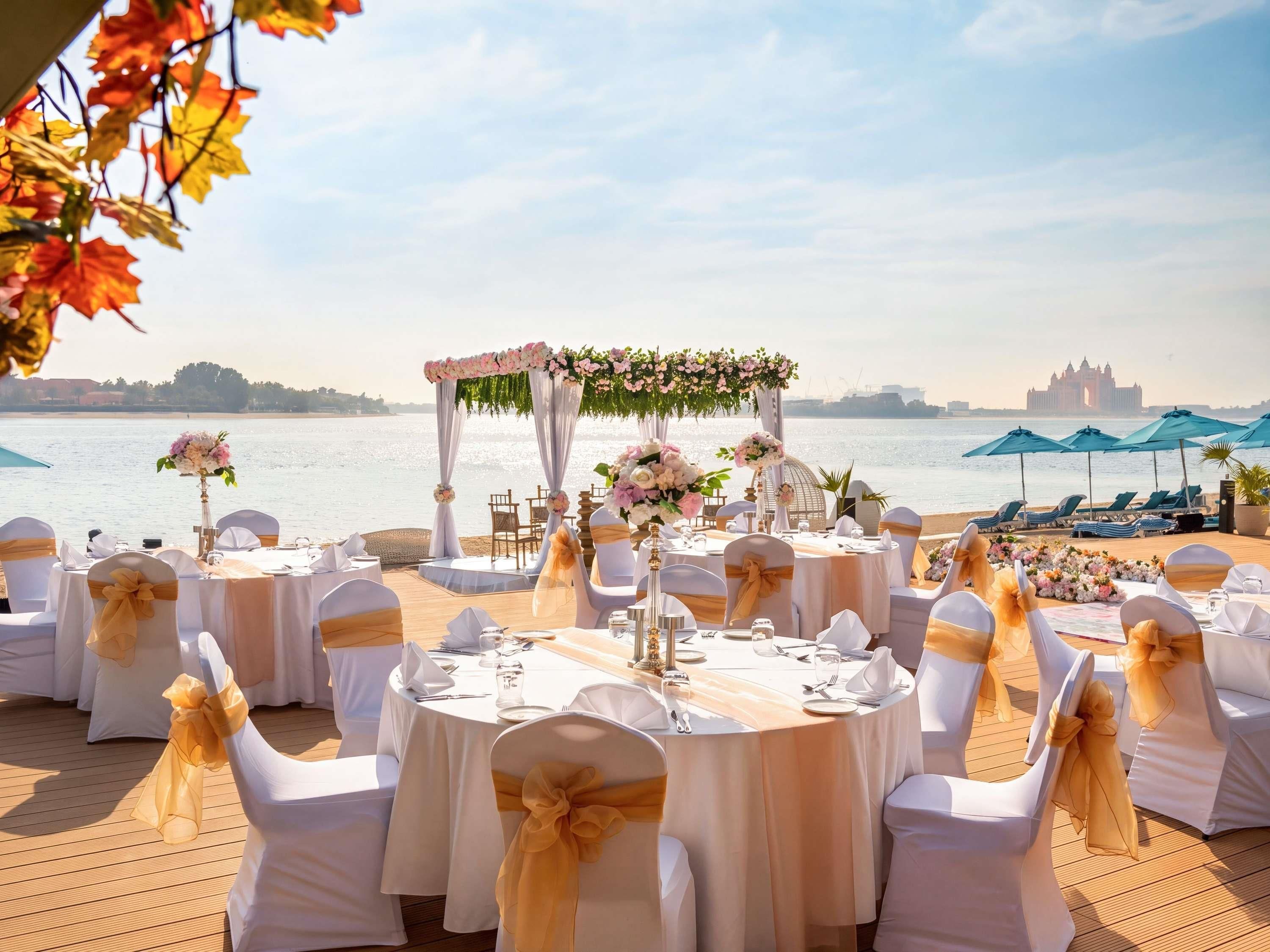 A wedding reception setup with round tables, white chairs with gold sashes, floral decorations, and a view of the sea and a castle in the background.