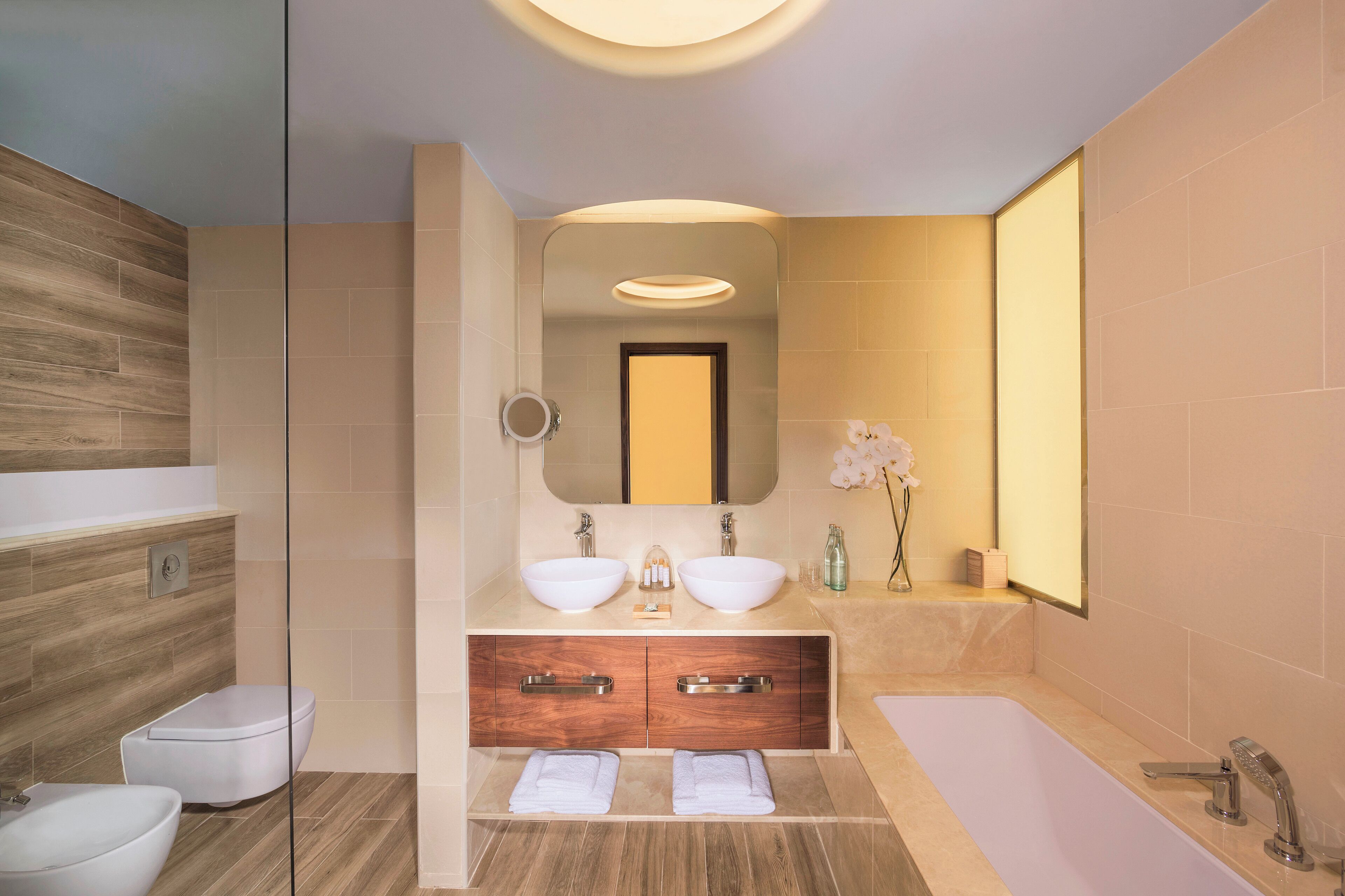 A modern bathroom with two sinks, a bathtub, and a toilet.