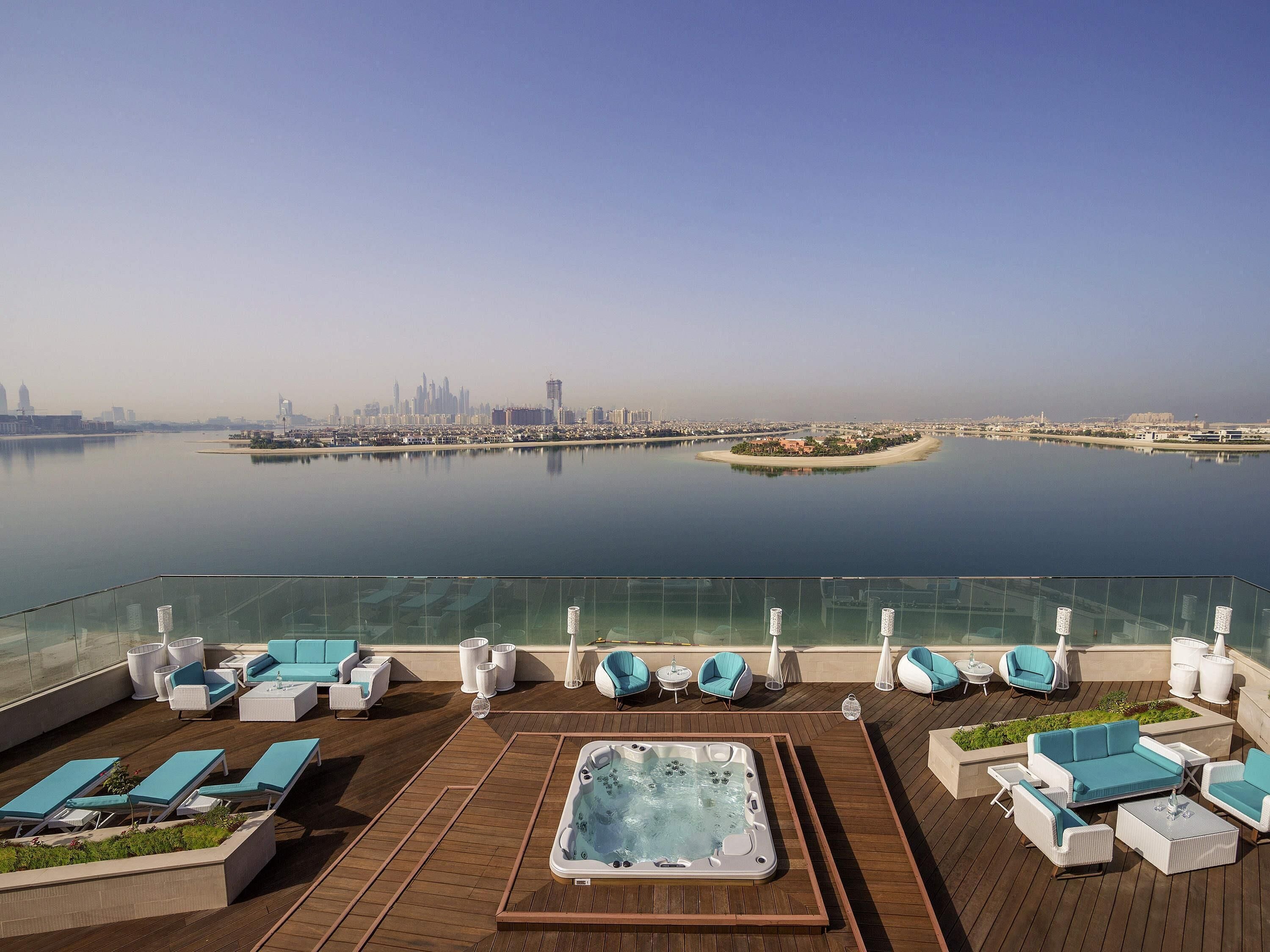 Terraza en la azotea con jacuzzi, sillones de descanso y vistas de un horizonte urbano sobre un cuerpo de agua.