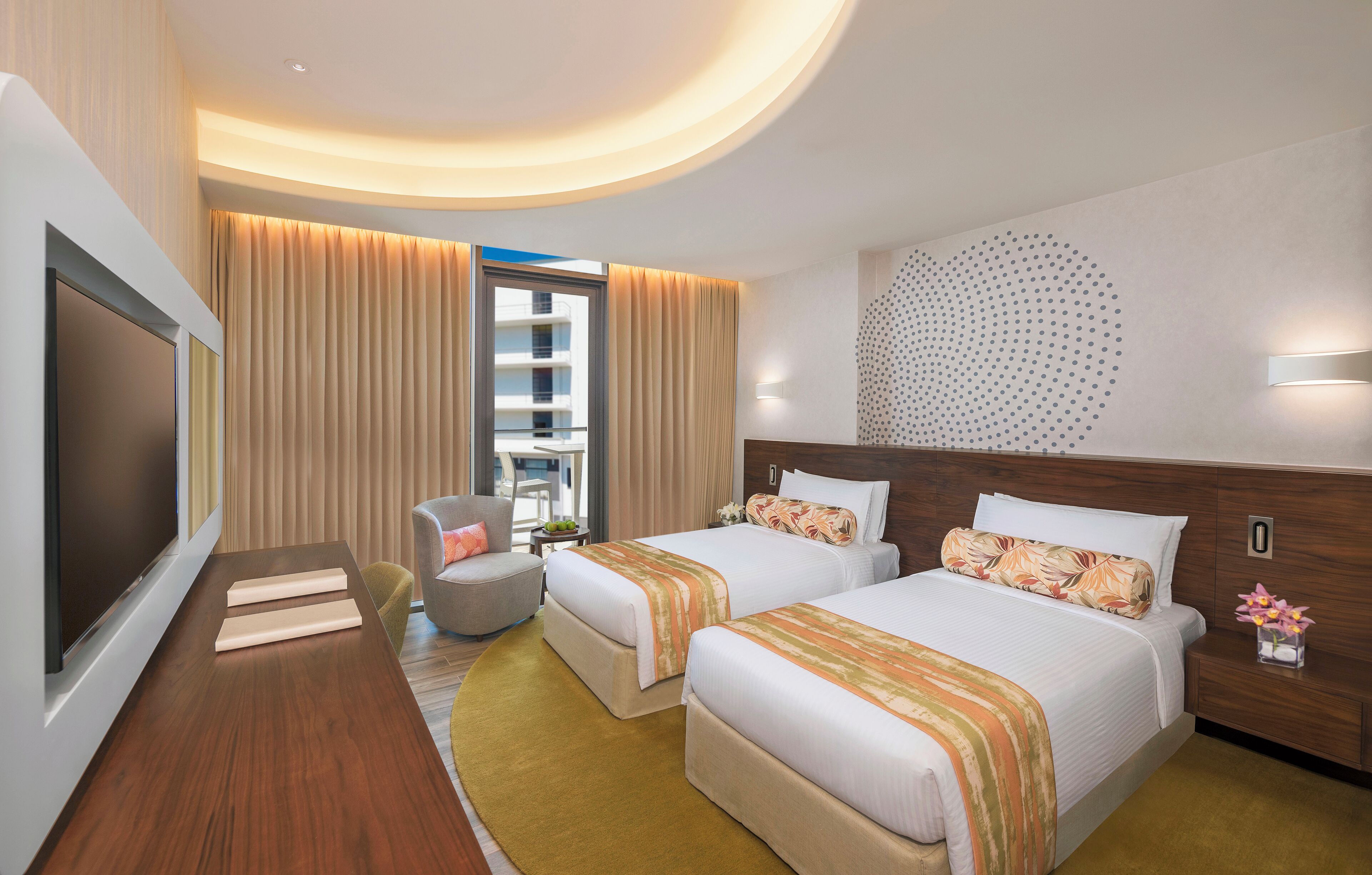 A hotel room with two beds, a TV, a desk, and a view of the building outside.