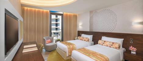A hotel room with two beds, a TV, a desk, and a view of the building outside.