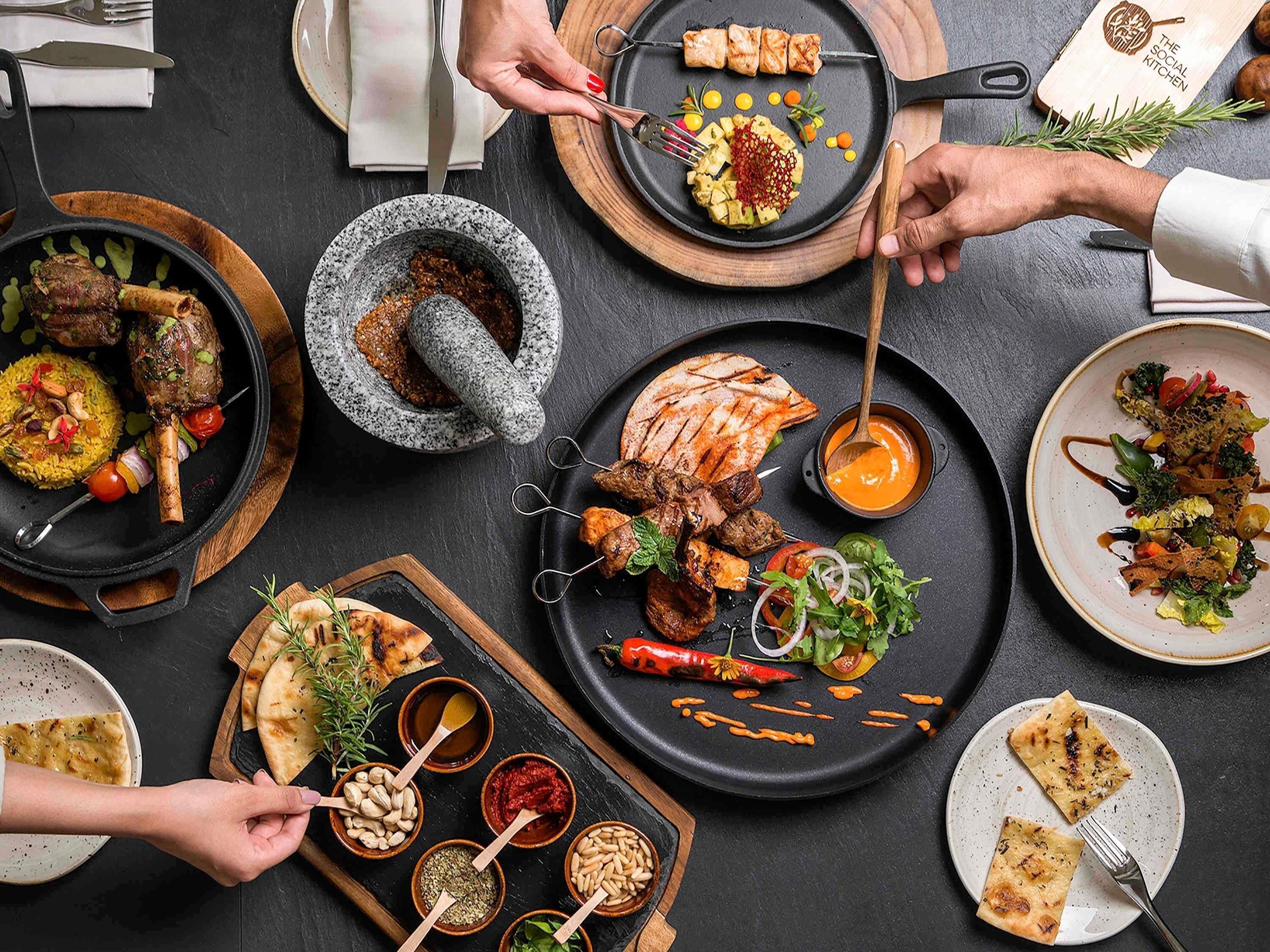 Una variedad de platos en una mesa de comedor, incluyendo carnes a la parrilla, verduras y panes planos.