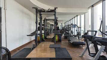 Une salle de sport équipée de divers appareils d’exercice, notamment des tapis de course et des appareils de musculation, disposés dans un espace vaste et bien éclairé, avec de grandes fenêtres.